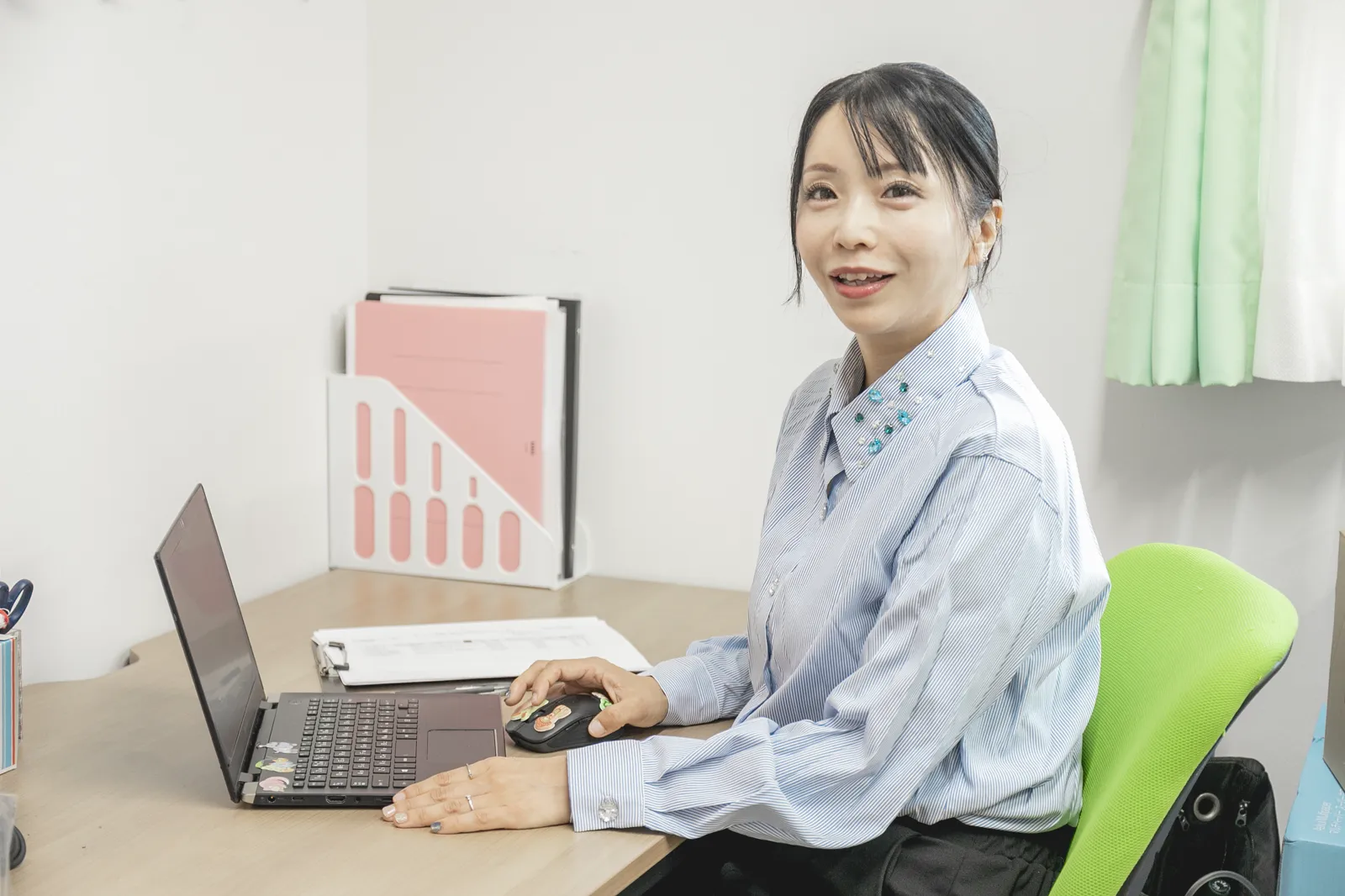 ノートパソコンの前で、こちらを向いて微笑む稲津